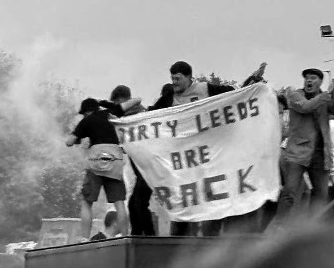 Black and white Leeds supporters holding a banner reading Dirty Leeds Are Back.