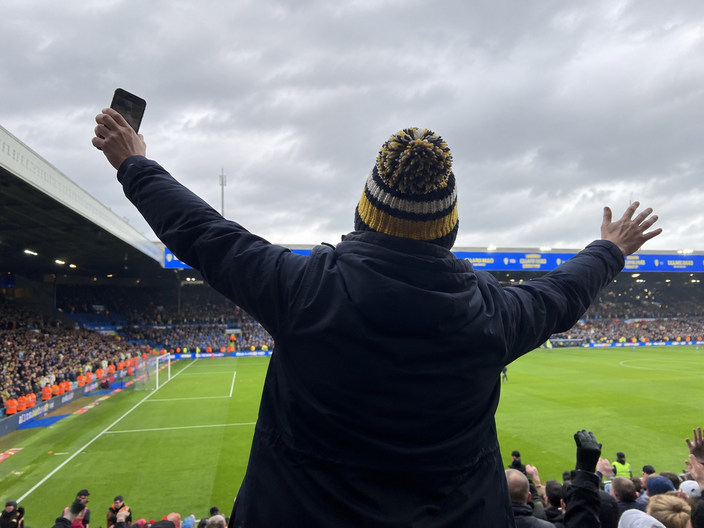 Leeds United Smiley Red Bull Emblem Striped Fur-Lined Bobble Hat – Elland Road setting.