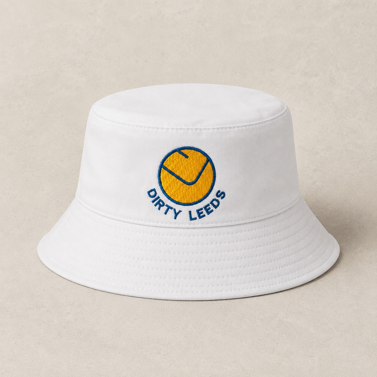 Front view of the white Dirty Leeds® Leeds United Smiley Badge Bucket Hat with embroidered smiley badge and Dirty Leeds lettering.