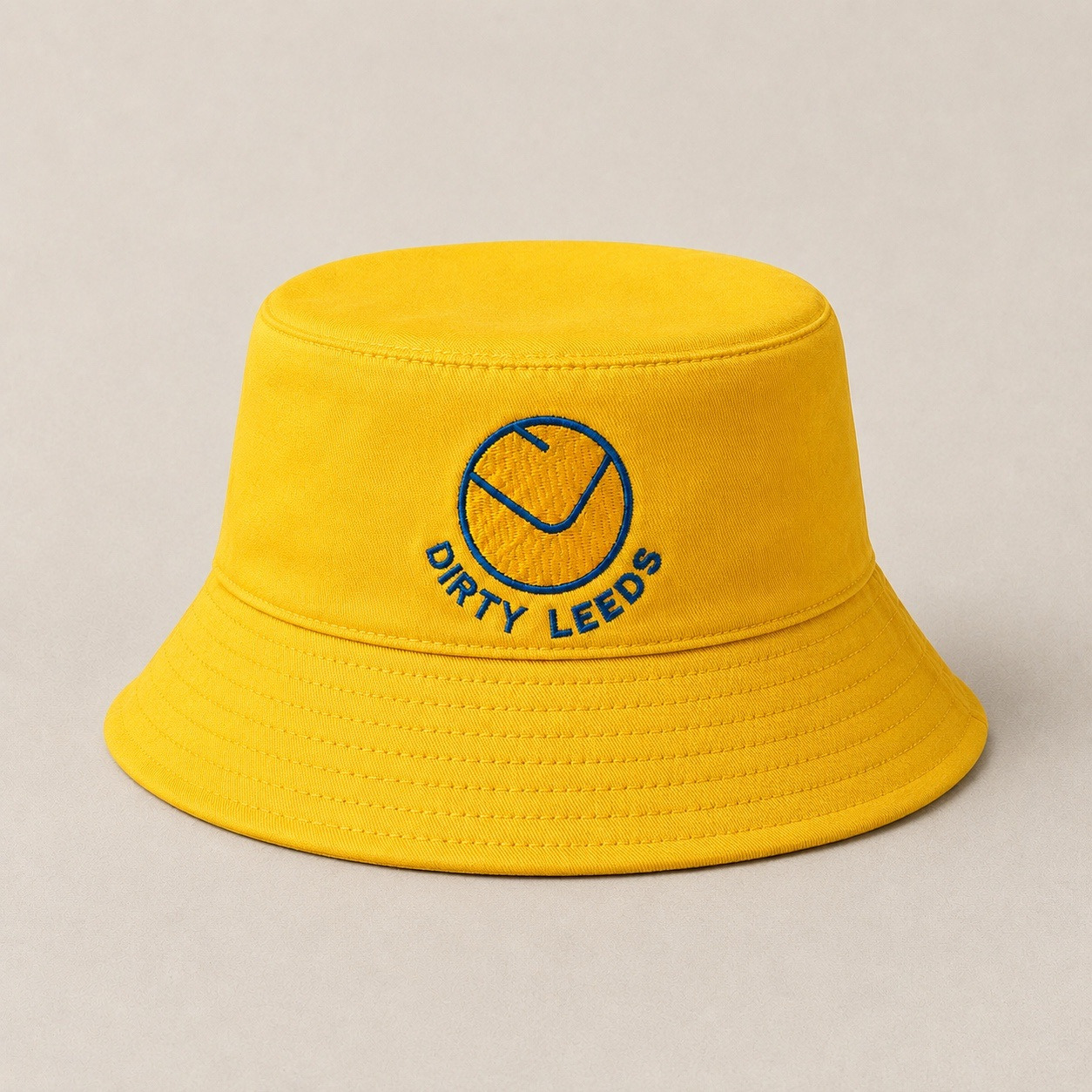 Front view of the yellow Dirty Leeds® Leeds United Smiley Badge Bucket Hat with embroidered smiley badge and Dirty Leeds lettering.