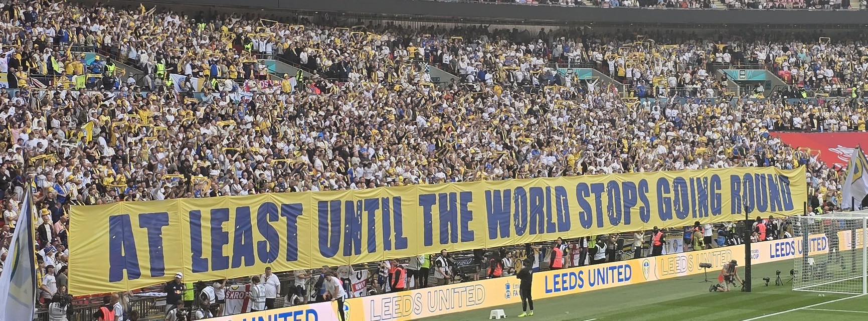 Leeds supporters holding a huge yellow and blue banner reading At least until the world stops going round.