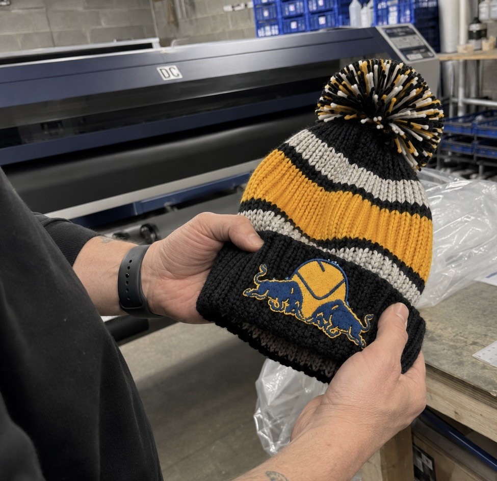 Hands holding a Dirty Leeds bobble hat inside the West Yorkshire mill where products are sourced.